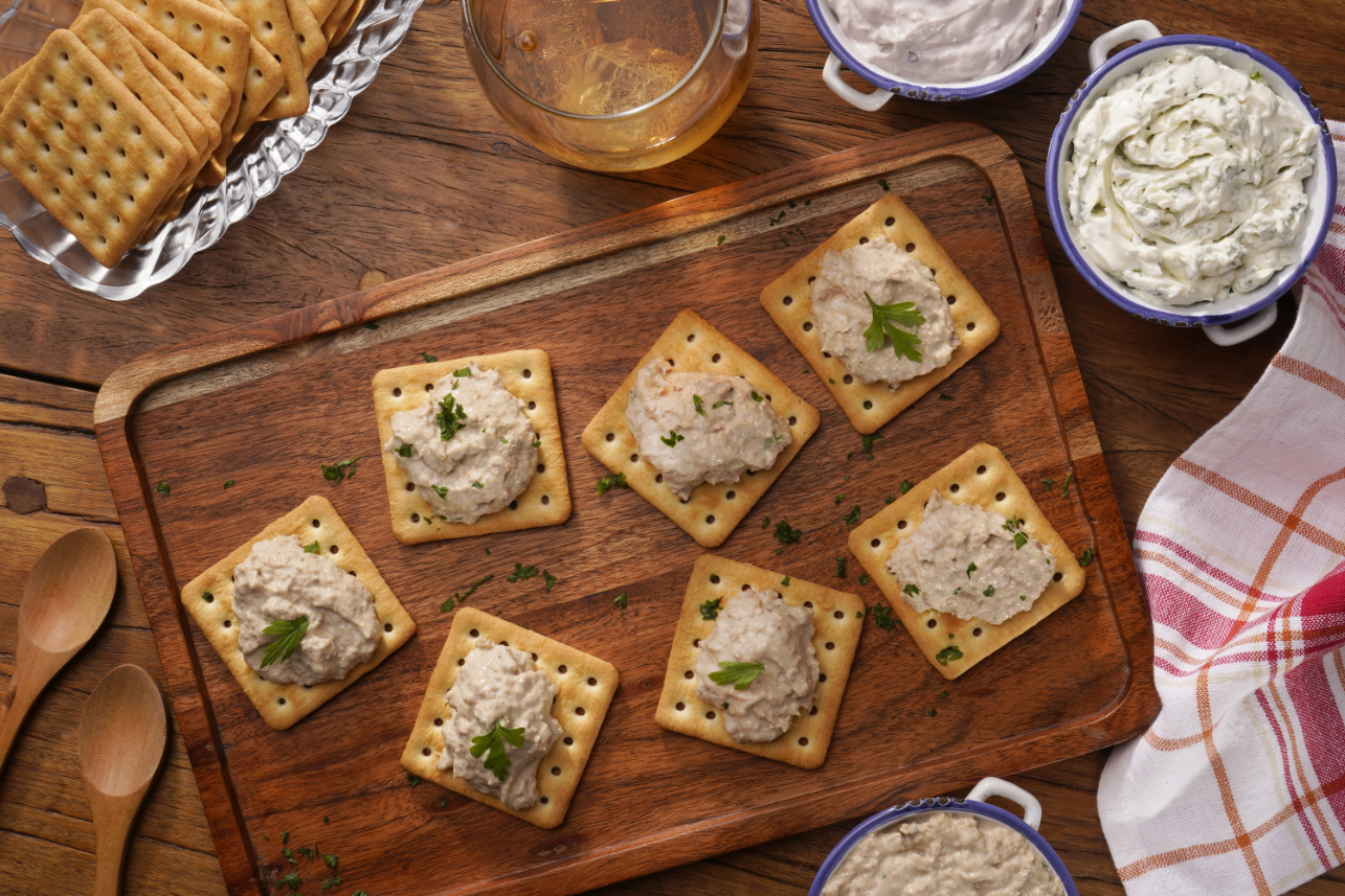 Biscoitos cream cracker sobre tábua de madeira com porções de patê e salsinha.