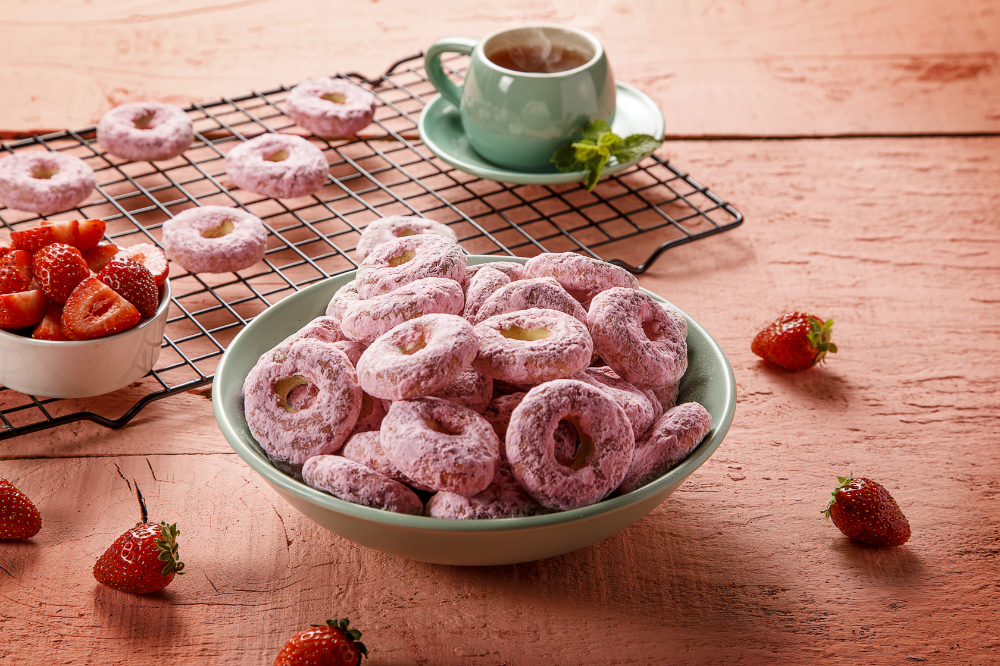 Pote com biscoito calda sabor morango, exibido sobre fundo rosa e xícara de chá