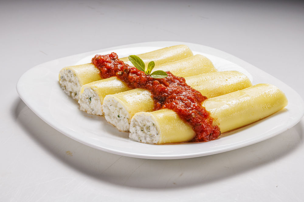 Prato de macarrão canelloni recheados com patê branco e cobertos em molho vermelho.