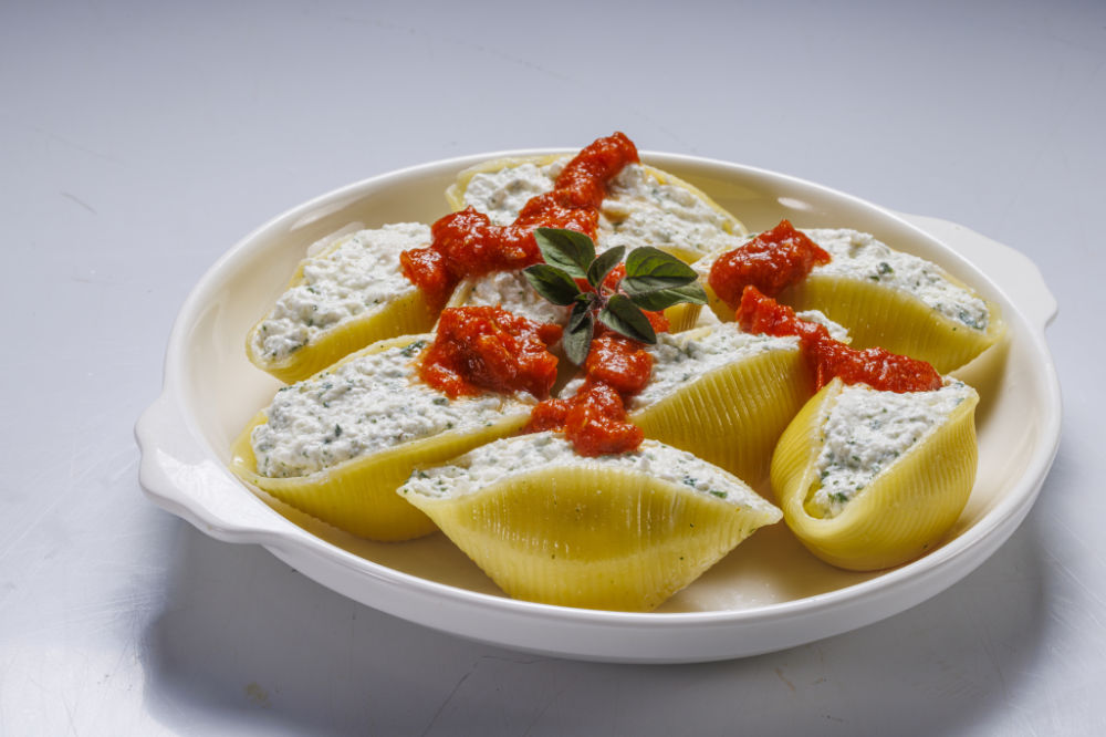 Prato de macarrão conchiglioni, recheado com patê branco e coberto em molho vermelho.