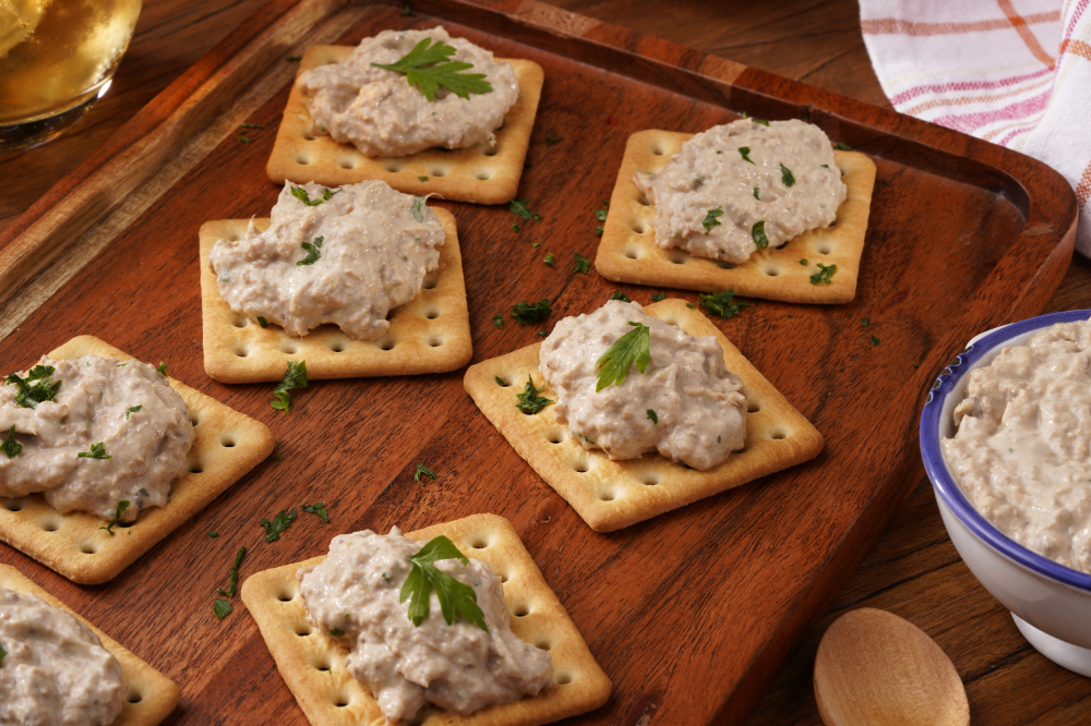 Biscoitos cream cracker sobre tábua de madeira com porções de patê e salsinha.