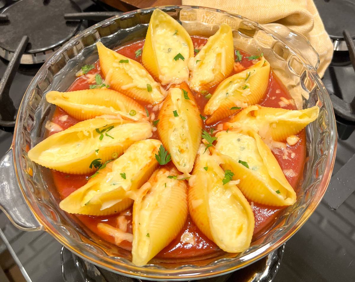 Travessa com conchiglioni recheados de queijo e cobertos por molho vermelho e cebolinha.