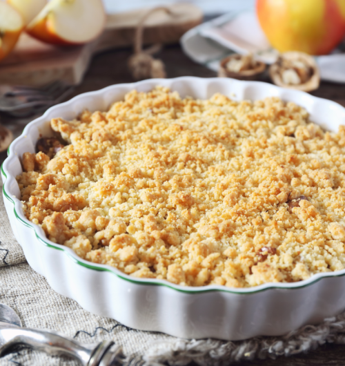 Crumble de maçã assado, com cobertura de biscoito maisena, sobre fundo desfocado.