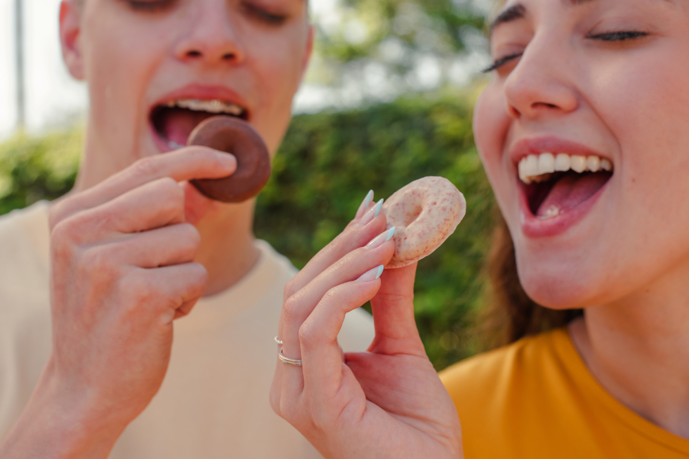 Casal compartilhando donuts sabor chocolate ao leite, em ambiente claro externo
