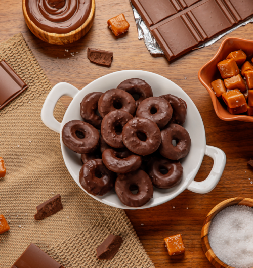 Prato branco com donuts sabor chocolate amargo e cristais, sobre mesa de madeira.