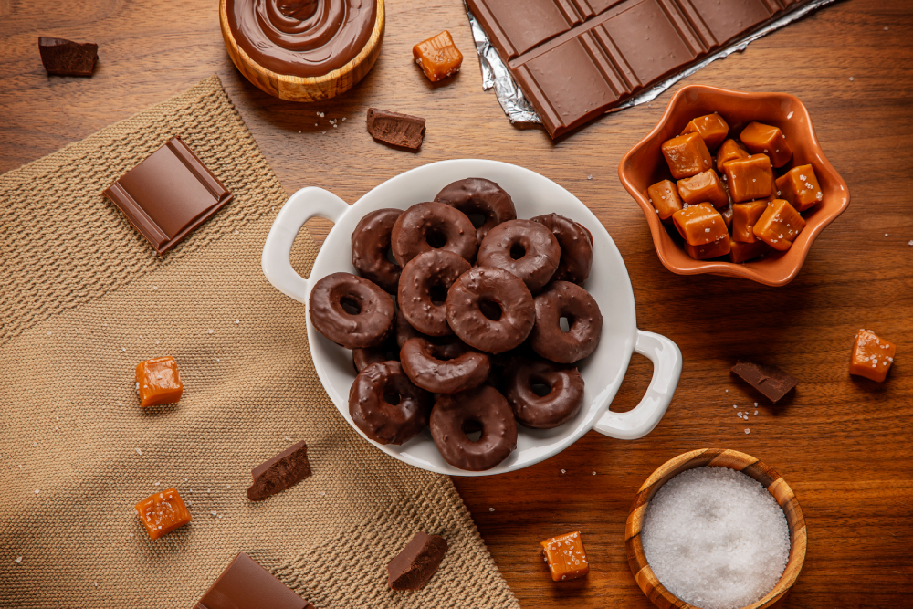 Prato branco com donuts sabor chocolate amargo e cristais, sobre mesa de madeira.