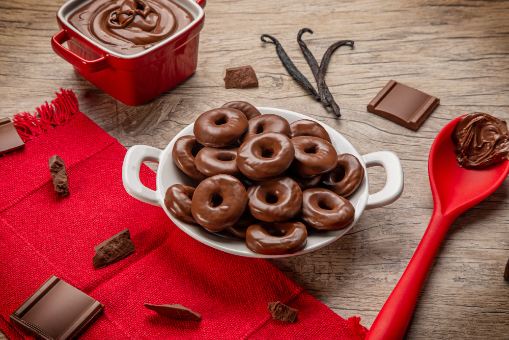 Prato branco com donuts sabor chocolate ao leite, sobre mesa de madeira.