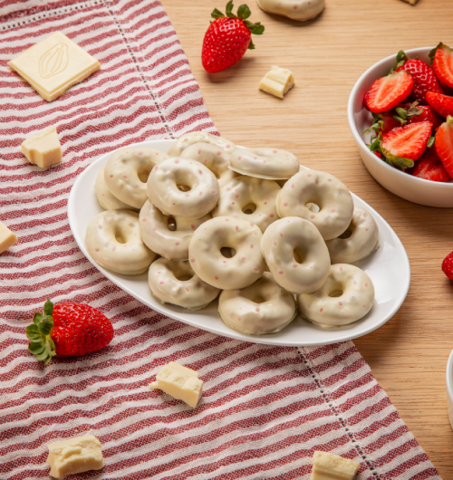 Prato branco com donuts sabor chocolate branco e morango, sobre mesa de madeira.