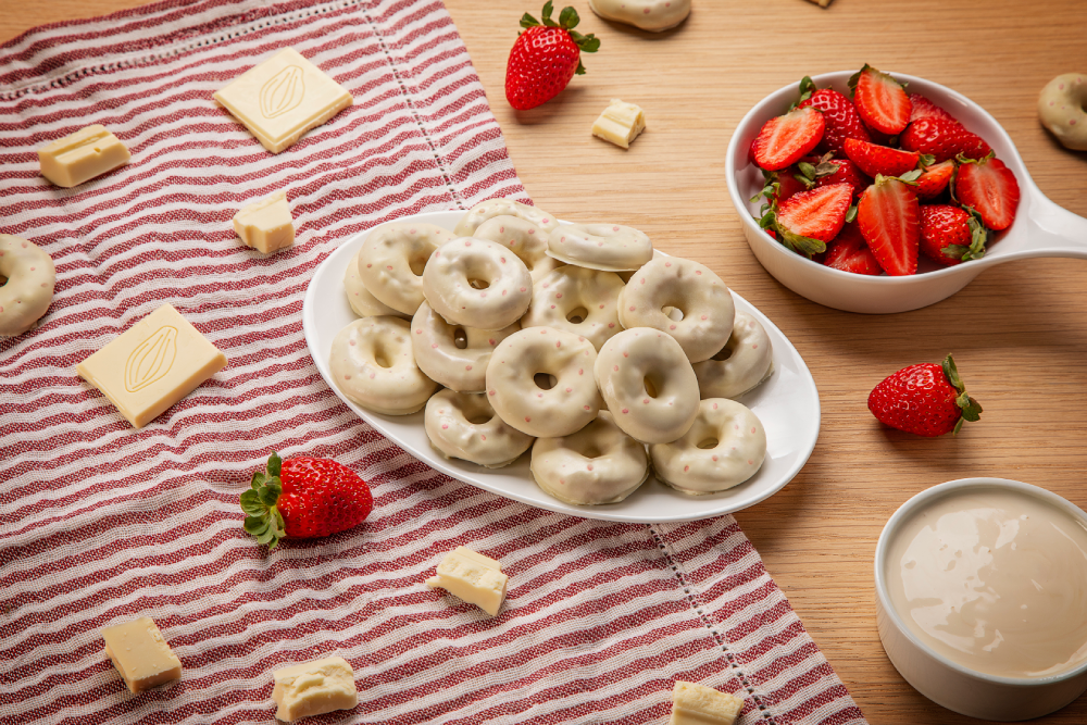 Prato branco com donuts sabor chocolate branco e morango, sobre mesa de madeira.