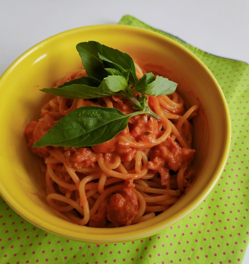 Prato de espaguete, coberto com molho vermelho, linguiça toscana e manjericão fresco.