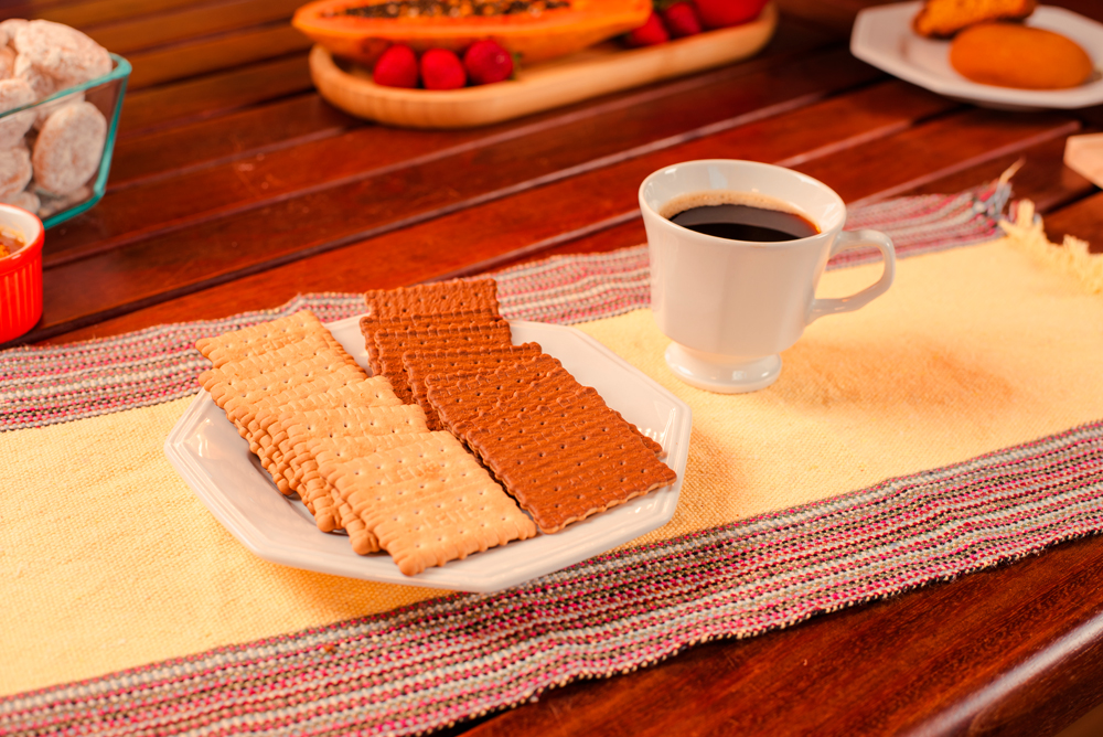Prato branco com biscoitos Doble, servidos sobre mesa de madeira ao lado da xícara de café