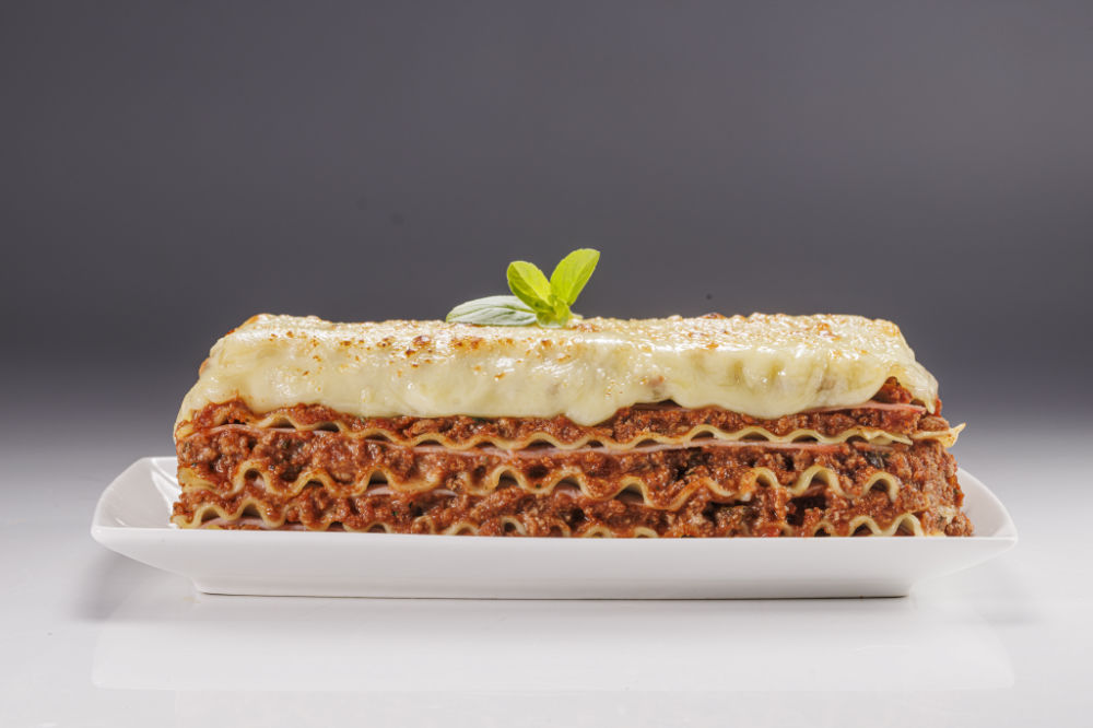 Porção de lasanha em camadas de massa, molho e queijo, servida em prato branco.