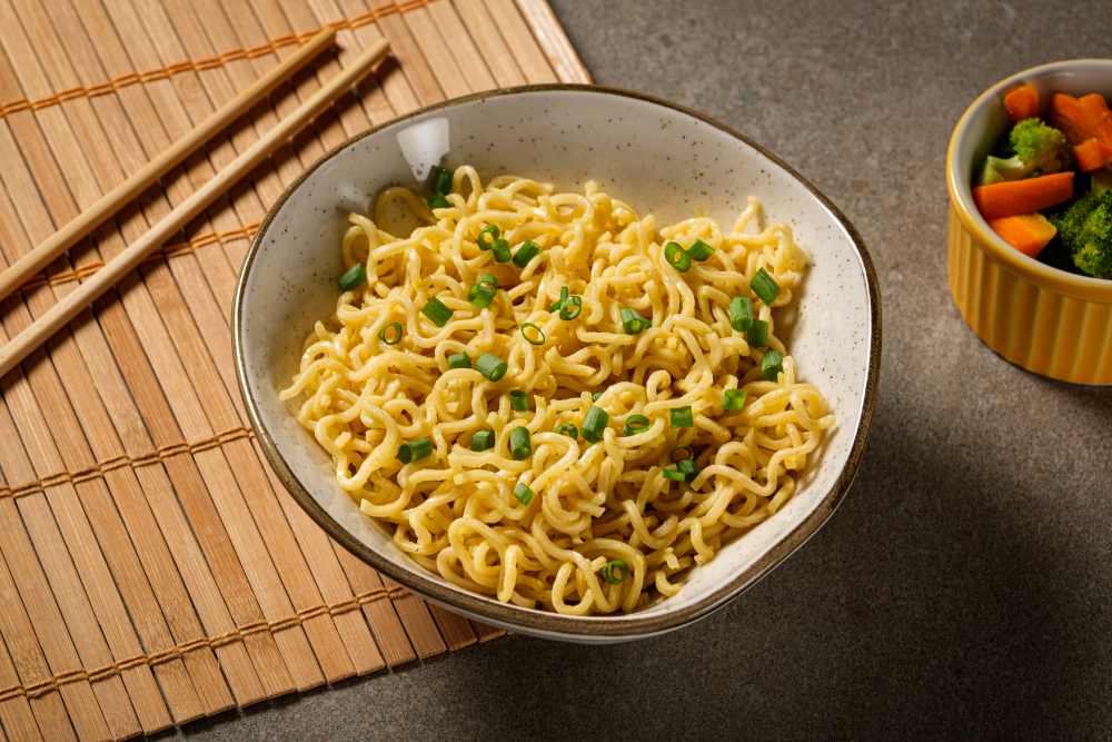 Tigela de macarrão instantâneo sabor galinha, com cebolinha, sobre mesa de madeira.