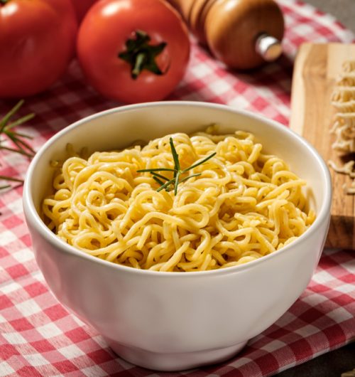 Tigela de macarrão instantâneo sabor galinha, com alecrim, sobre mesa de madeira.
