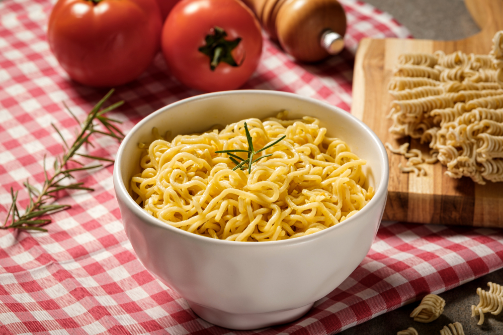 Tigela de macarrão instantâneo sabor galinha, com alecrim, sobre mesa de madeira.