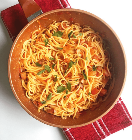 Panela com macarrão grano duro servido ao molho de tomate, acompanhado com ervas, sobre mesa clara