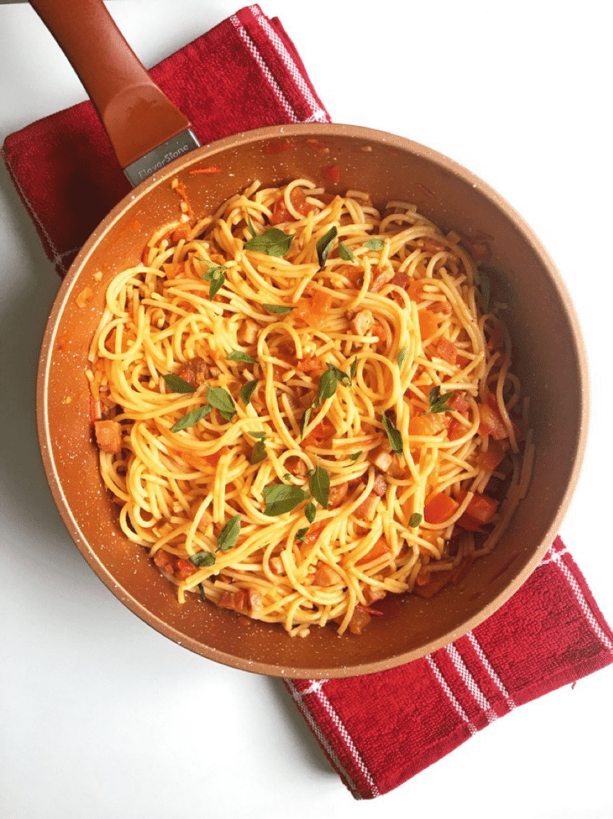 Panela com macarrão grano duro servido ao molho de tomate, acompanhado com ervas, sobre mesa clara