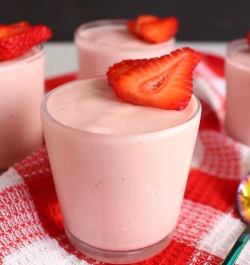 Taça com mousse de morango com rosca de calda, decorado com morangos, sobre fundo desfocado.