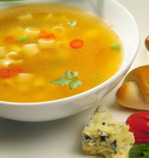 Prato fundo de sopa, com tomates, salsa, queijo gorgonzola e pão, dispostos sobre fundo claro