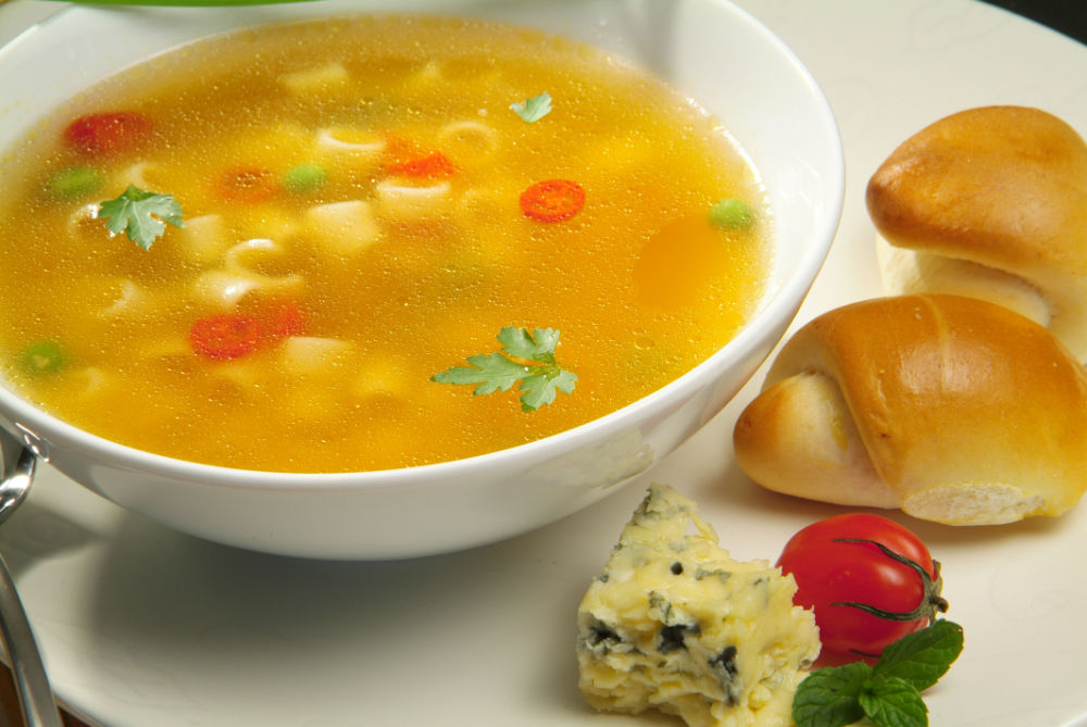 Prato fundo de sopa, com tomates, salsa, queijo gorgonzola e pão, dispostos sobre fundo claro