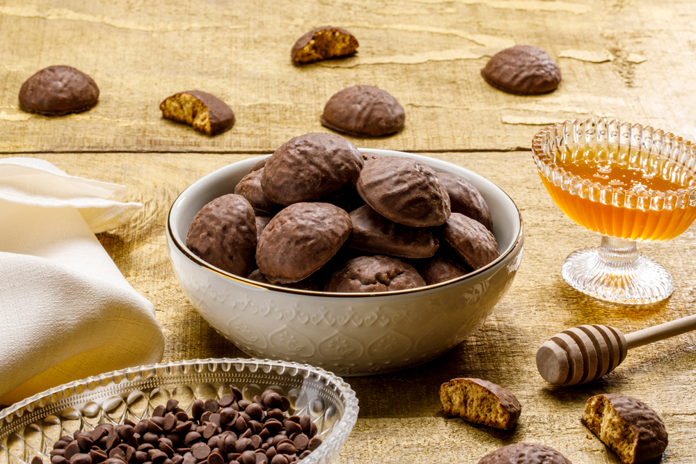 Pedaços de pão de mel cobertos com chocolate, dispostos em pote branco sobre mesa de madeira.