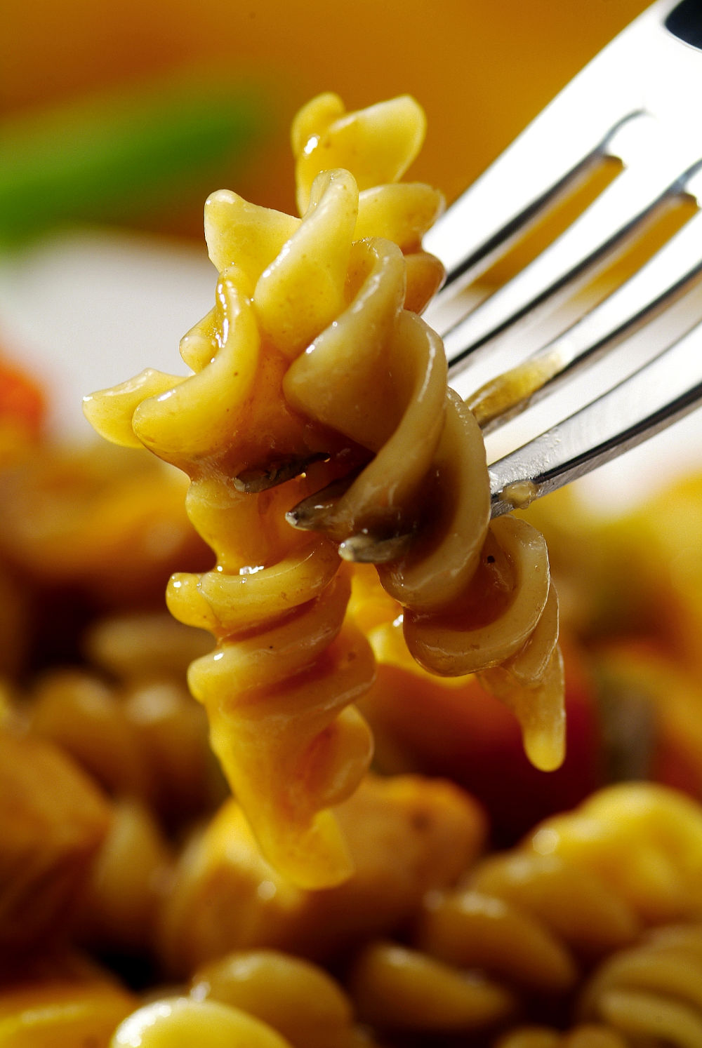 Garfo segurando macarrão parafuso coberto em molho, sobre fundo desfocado