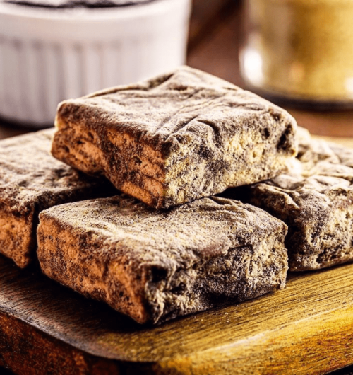 Palha italiana de café com biscoito maisena, cobertos com açúcar, dispostos sobre mesa de madeira.