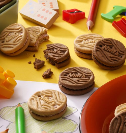 Biscoitos recheados, sabores chocolate e morango, dispostos em mesa com brinquedos.