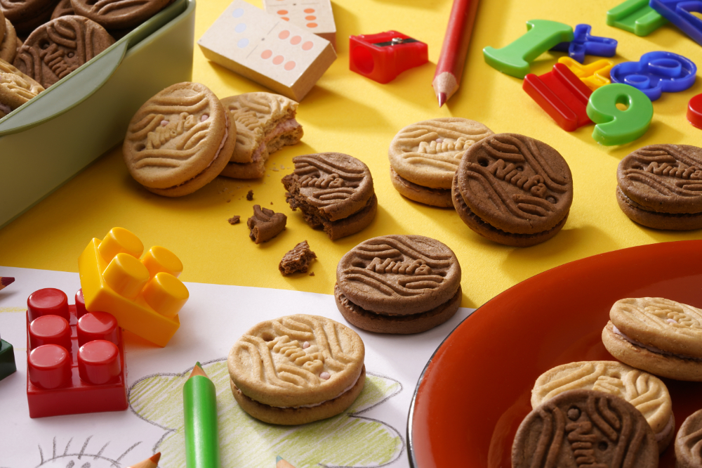 Biscoitos recheados, sabores chocolate e morango, dispostos em mesa com brinquedos.