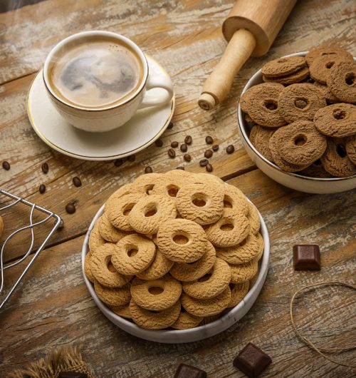 Biscoitos rosca de leite, dispostos em potes brancos sobre mesa de madeira