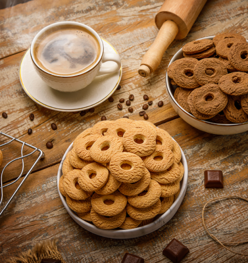 Biscoitos rosca de leite, dispostos em potes brancos sobre mesa de madeira.