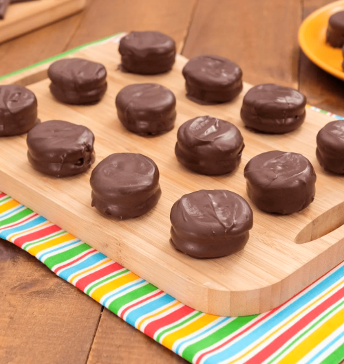 Alfajor feito com rosquinhas recheadas e cobertas por chocolate, servido em tábua de madeira, com pedaços cortados mostrando o recheio.