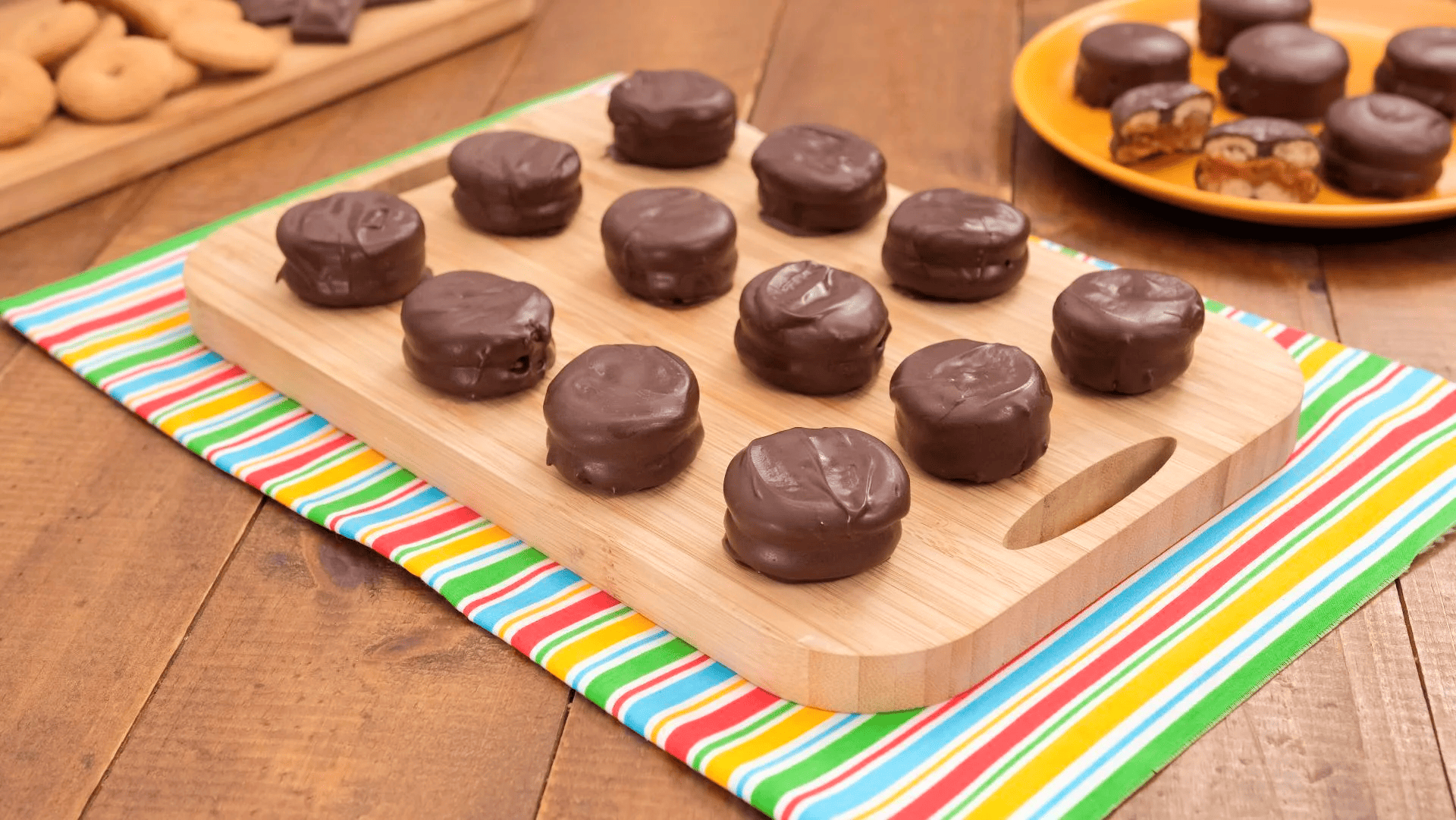 Alfajor feito com rosquinhas recheadas e cobertas por chocolate, servido em tábua de madeira, com pedaços cortados mostrando o recheio.