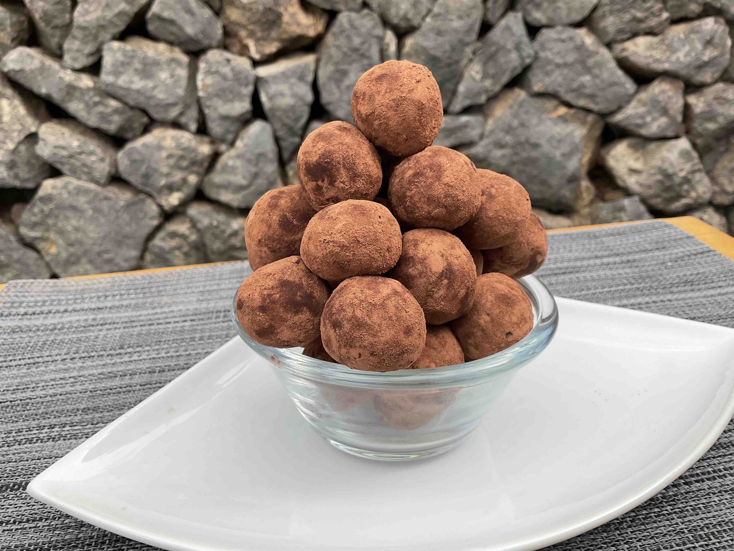 Pote com trufas de tiramisù feitas com biscoito champanhe, cobertas com cacau em pó e dispostas em torre.