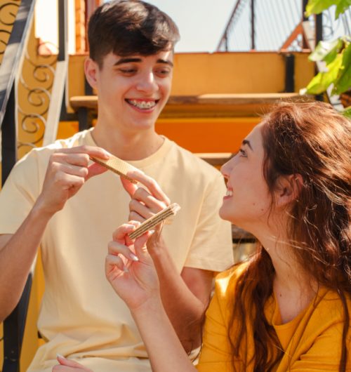 Casal jovem junto em ambiente iluminado, sorrindo enquanto compartilham wafers Ninfa sabor chocolate.