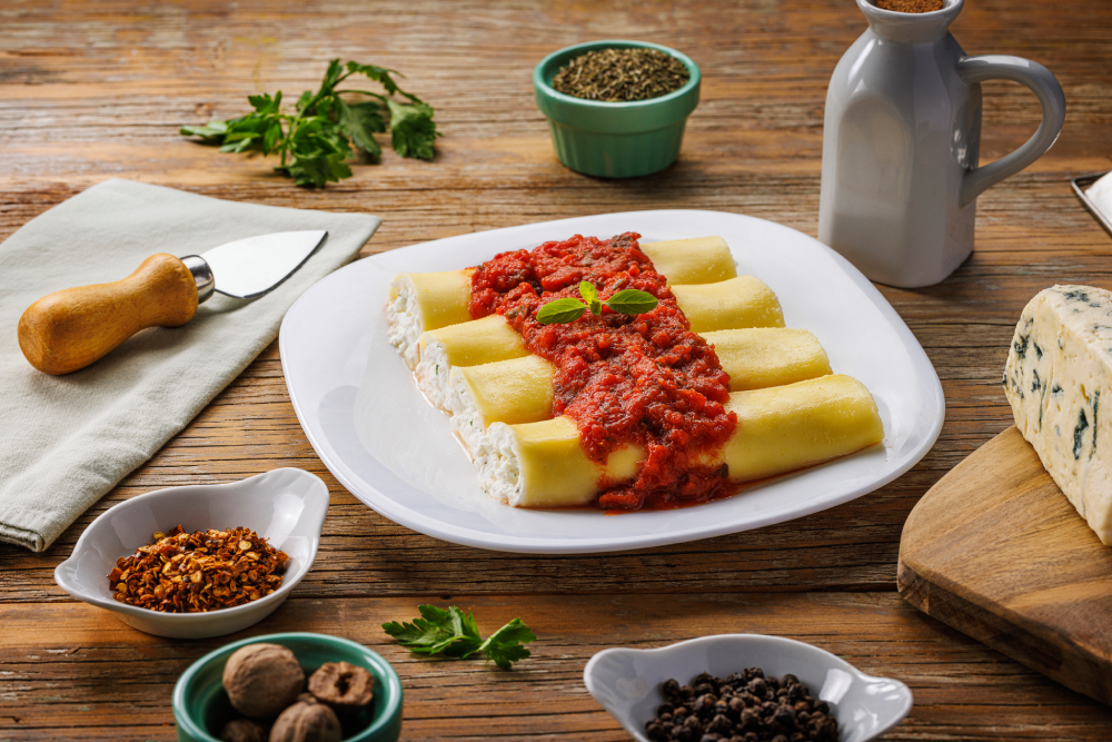 Prato de macarrão canelloni recheados com patê branco e cobertos em molho vermelho.