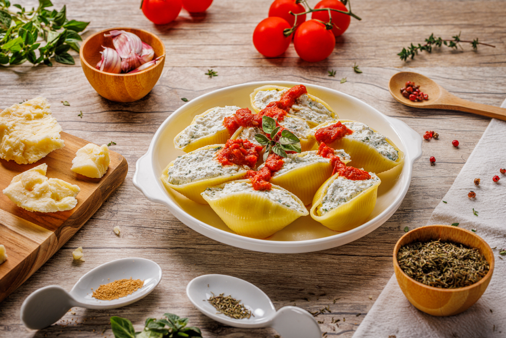 Prato de macarrão conchiglioni, recheado com patê branco e coberto em molho vermelho.