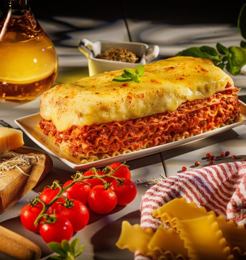 Porção de lasanha em camadas de massa, molho e queijo, servida em prato branco.