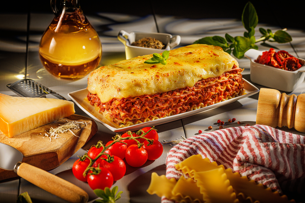 Porção de lasanha em camadas de massa, molho e queijo, servida em prato branco.