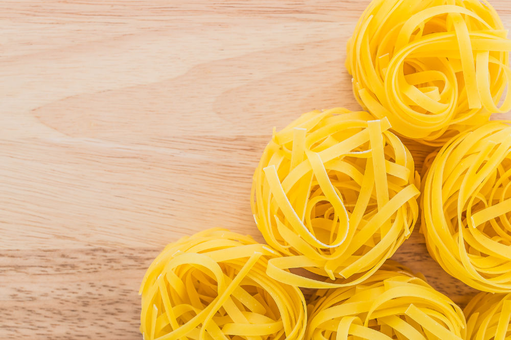 Macarrão fettuccine cru disposto em formato de ninho em superfície de madeira.